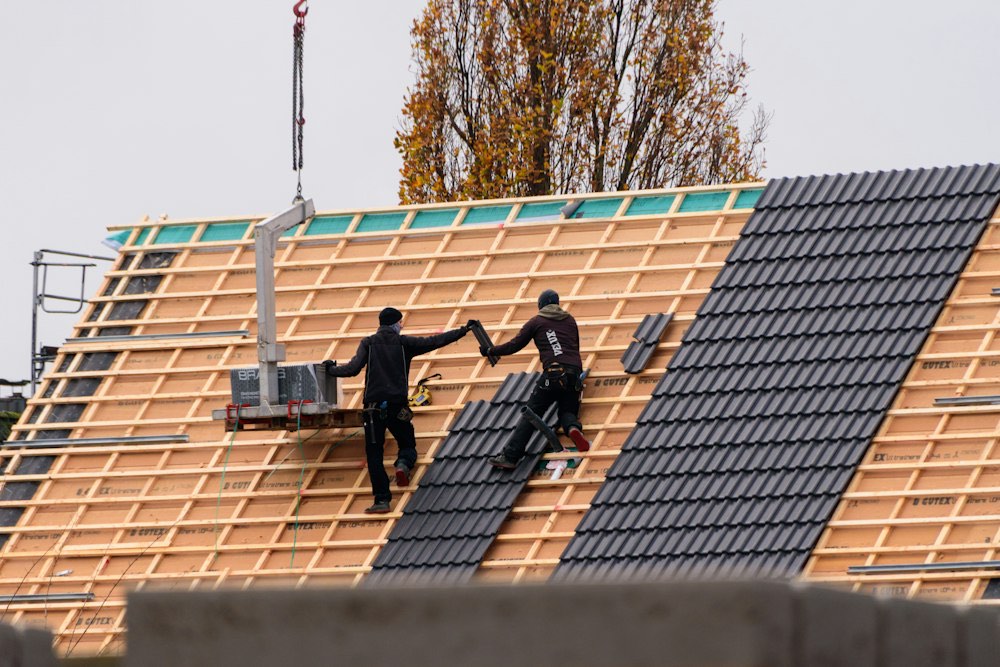 Twee dakwerkers leggen nieuwe donkere dakpannen op de panlatten van een hellend dak