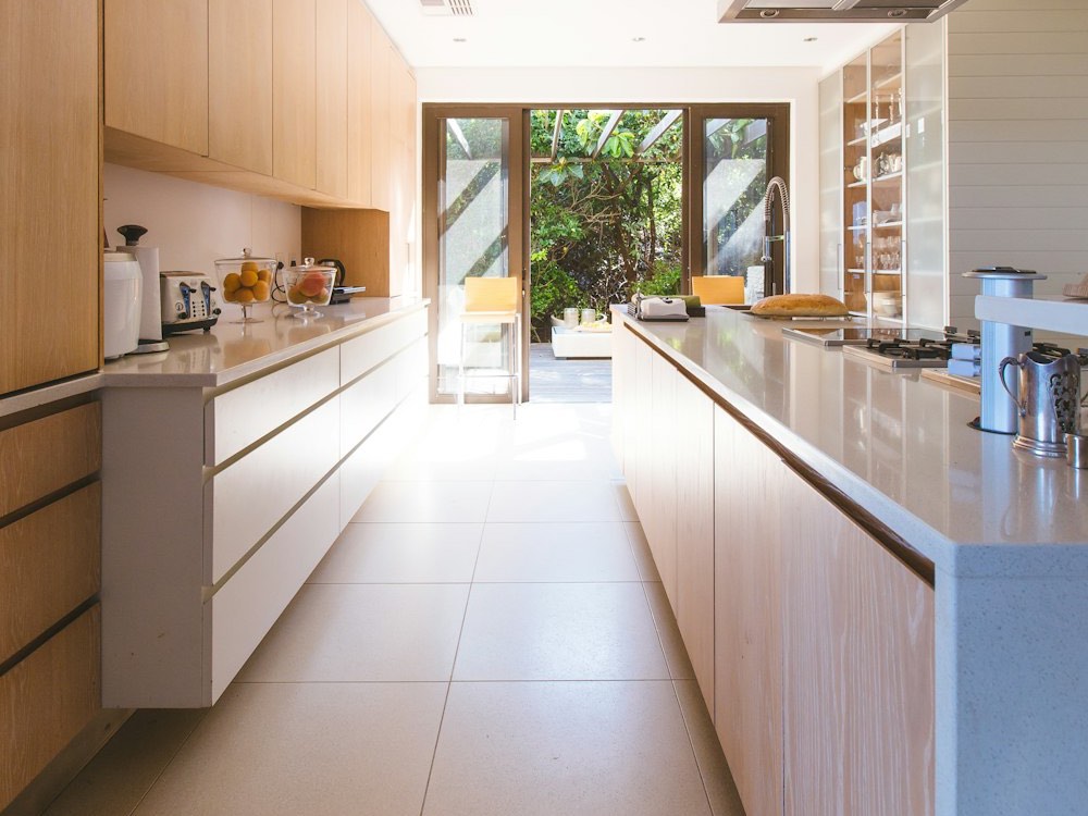 Lange keuken met houten kasten, een eiland met kookplaat en tuindeuren achteraan