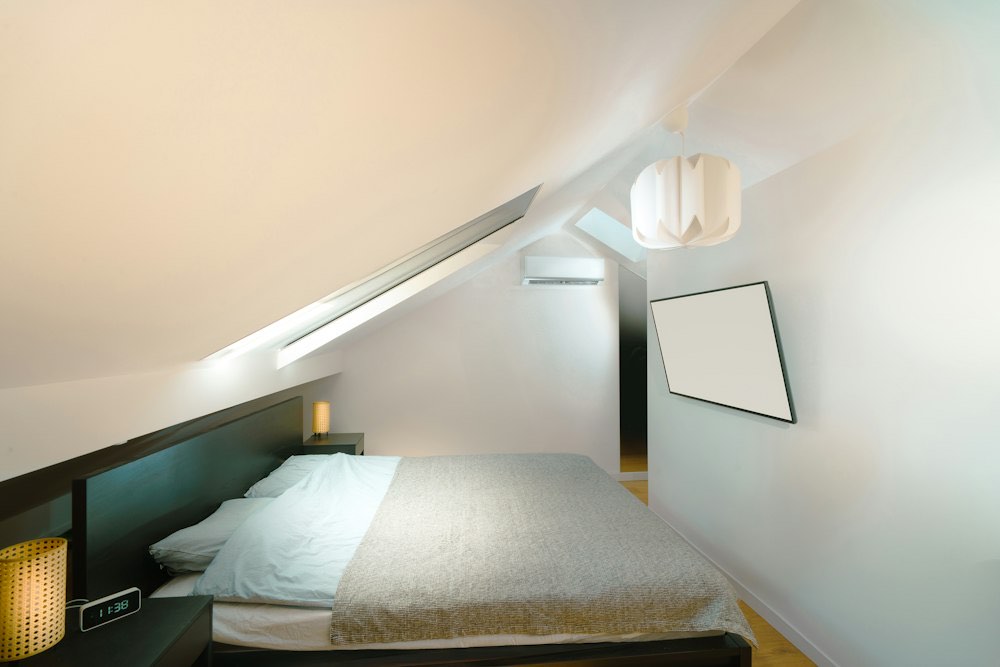 Lichte slaapkamer onder een schuin dak, met een bed en witte muren