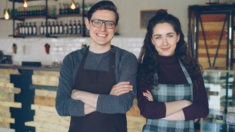 Twee uitbaters van een koffiebar staan met gekruiste armen voor hun toog