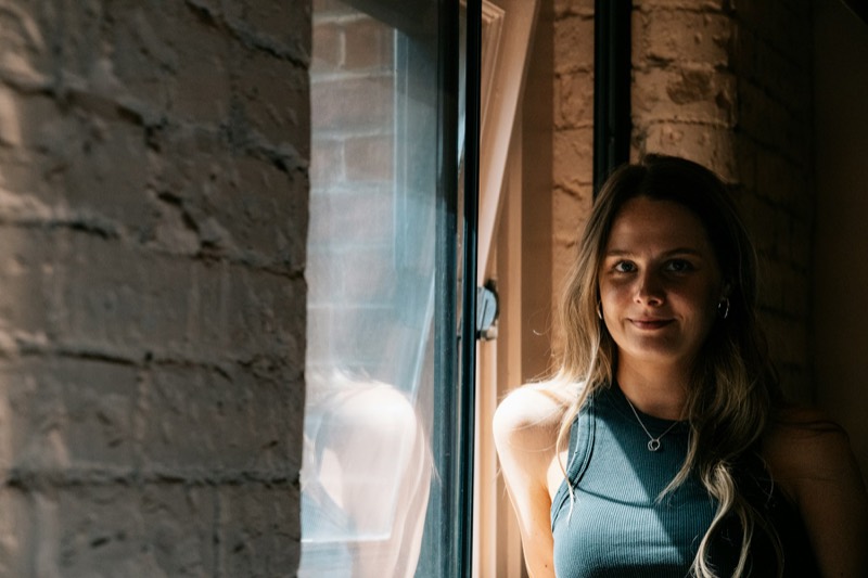 Jonge vrouw staat bij een open raam in een bakstenen muur en kijkt in de lens