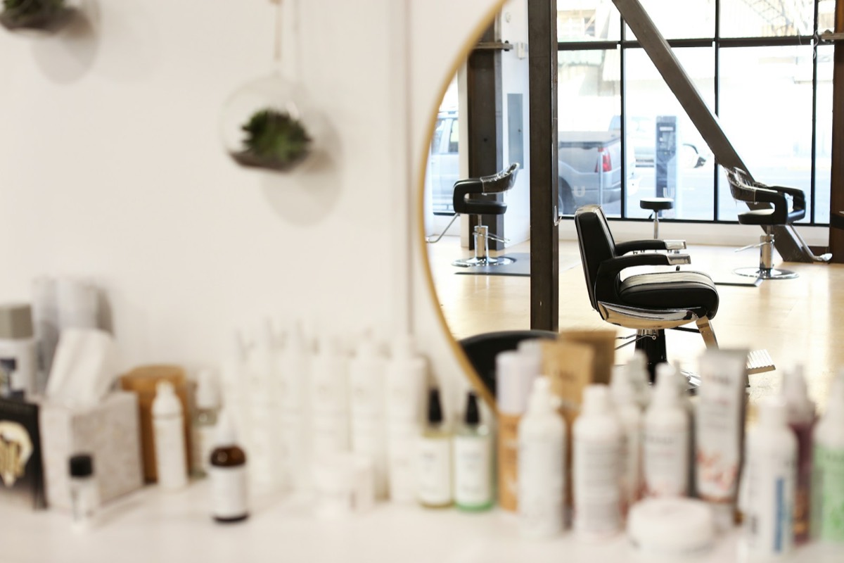 Kappersstoel voor een ronde spiegel, met een rek vol verzorgingsproducten op de voorgrond