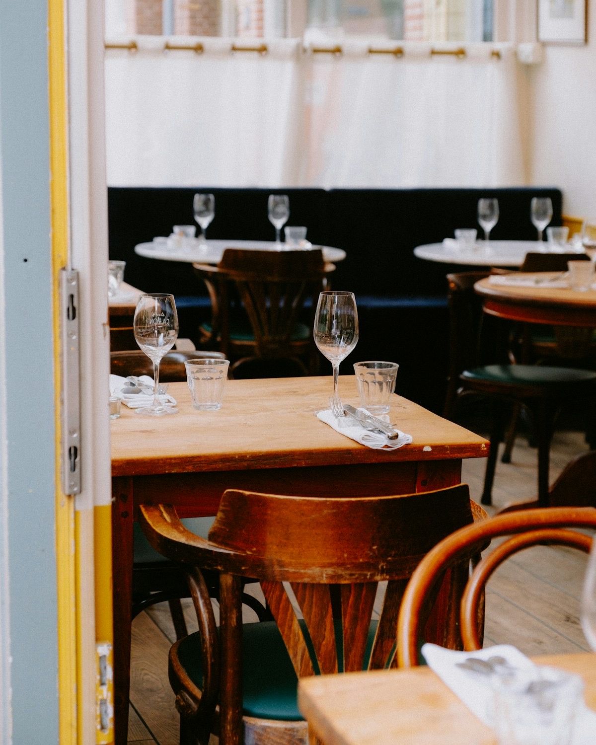 Gedekte houten tafels met wijnglazen en bistrostoelen in een lichte zaal